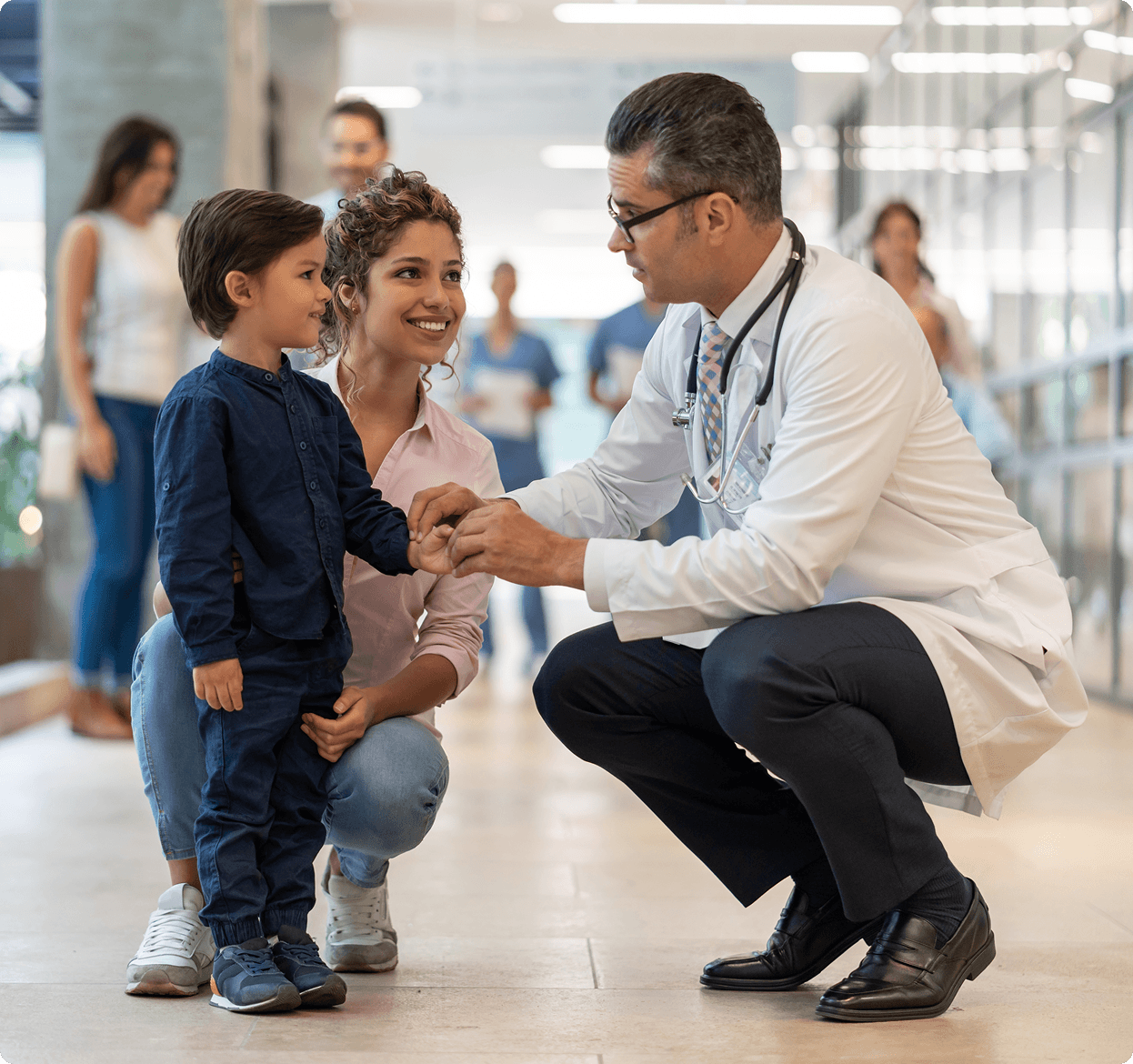 Male pediatrician crouching down to male toddler patient and their mother
